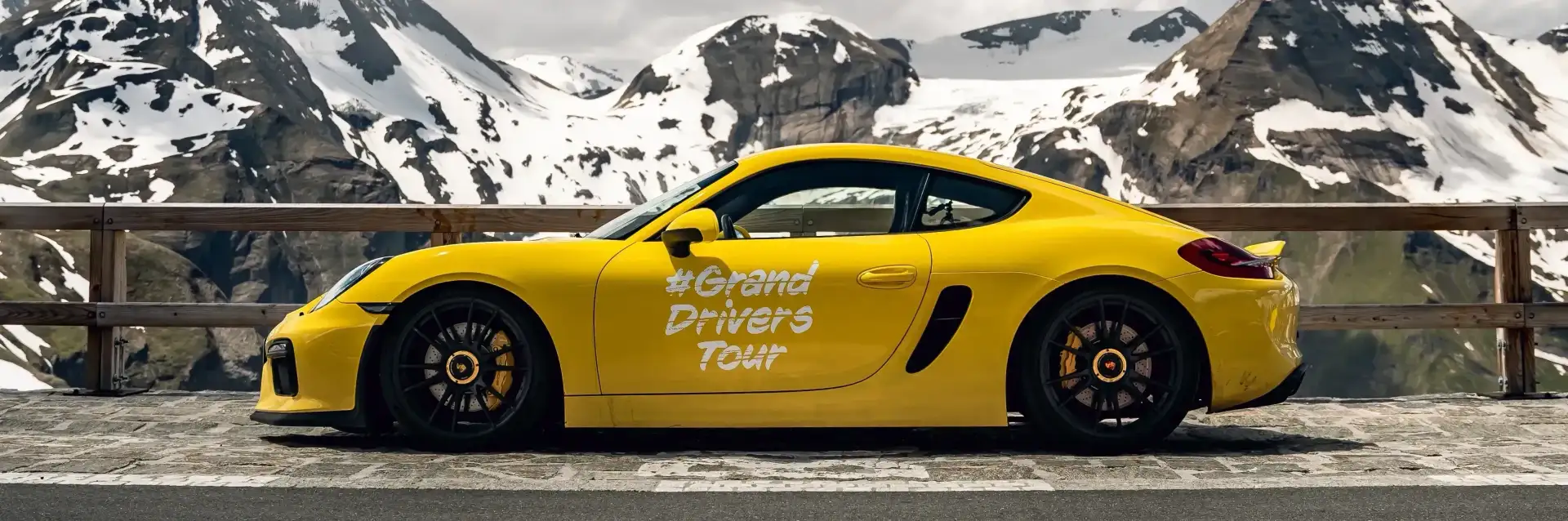 A yellow Porsche with lettering in front of a mountain relief.